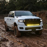 White 2026 RAM 1500 HEMI with 40in light bar PRO glowing yellow on a muddy off-road trail