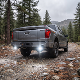 2022 Ford F-150 reverse light kit on a forest trail, white off-road light shining from both rear pods, rear three-quarter view