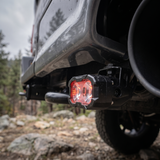 2025 Ford F-150 reverse light close-up, 20W PRO pod with red backlight on its powder coated bracket, forest trail