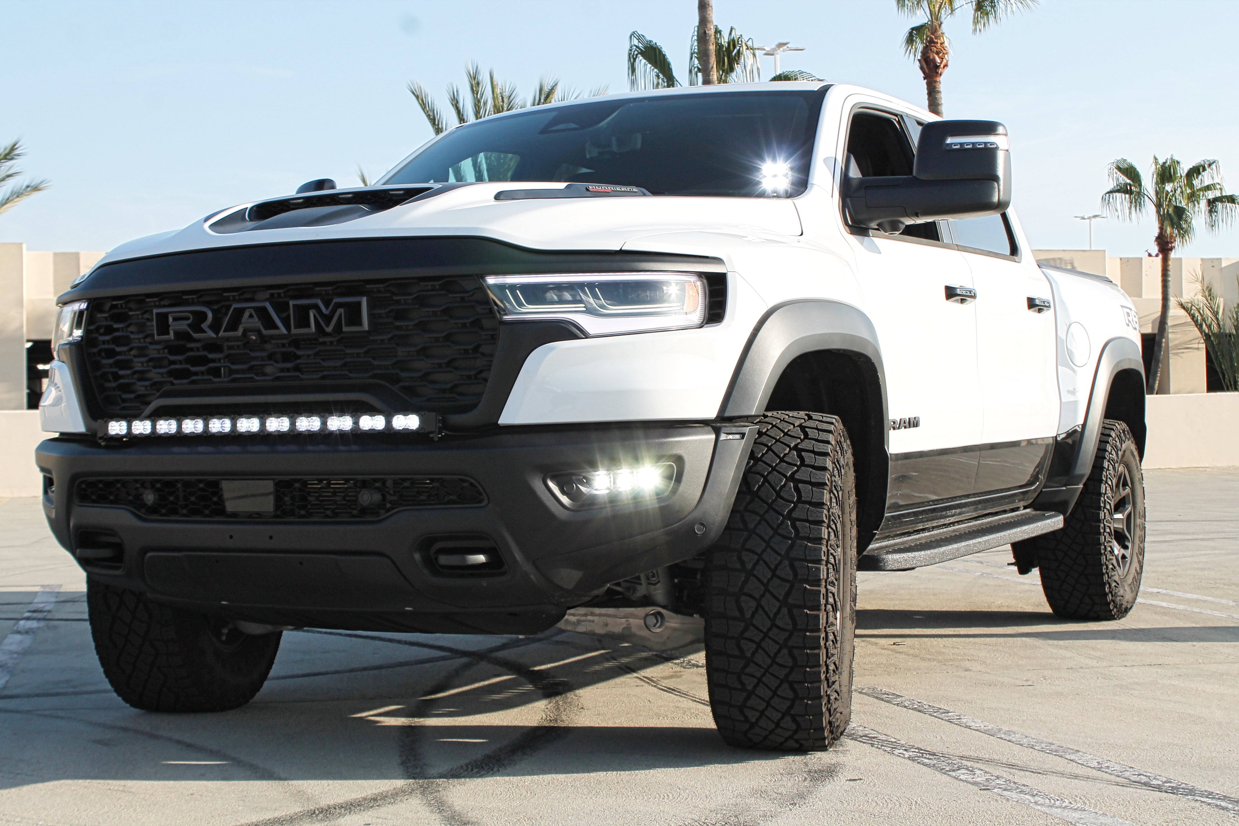 RAM RHO FOG Kit installed on 2025 RAM 1500; front view of white RAM with black RHO fog lights, bolt-on bracket, no cutting
