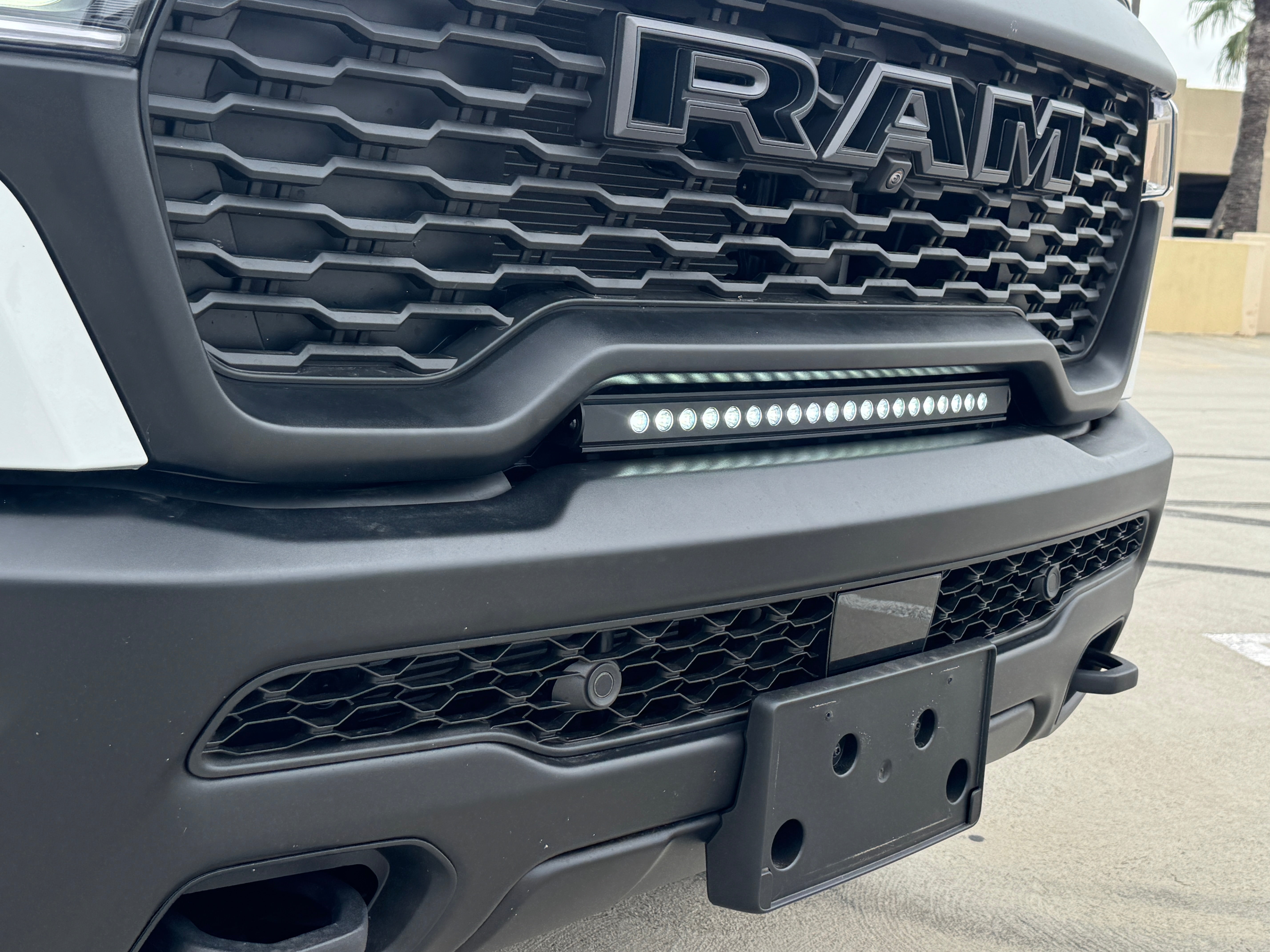 RAM RHO lightbar installed on 2025+ RAM 1500 Rebel, slim curved LED light between grille and bumper with black powder-coated metal bracket