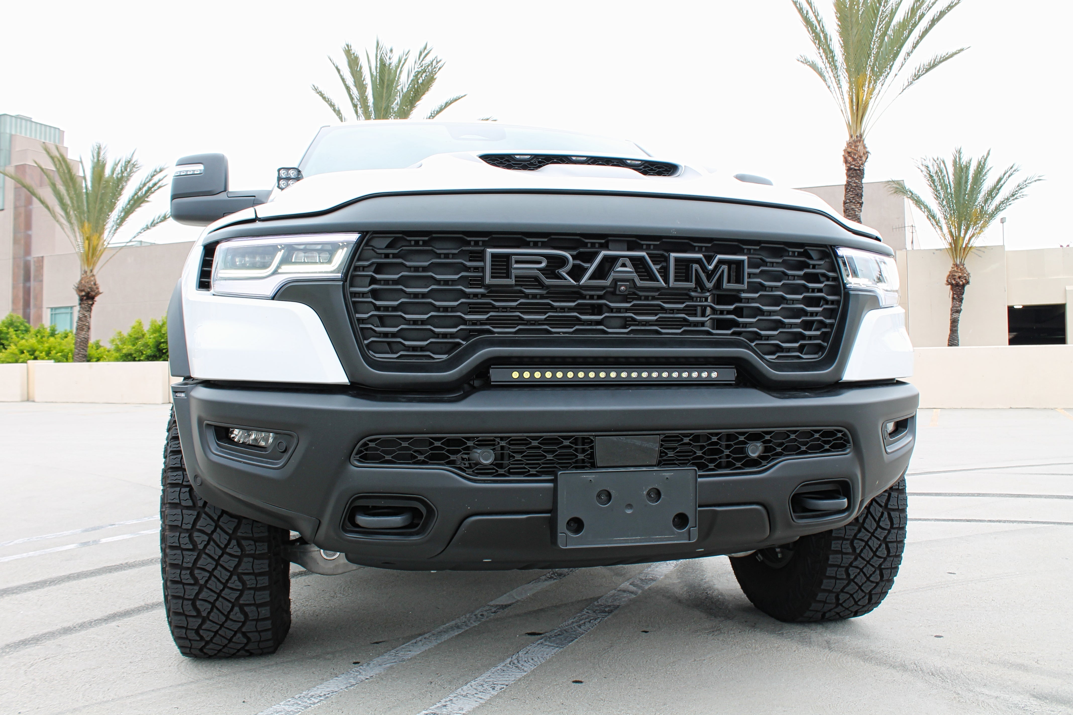 RAM RHO lightbar on 2025+ RAM 1500 Rebel — curved slim light bar between grille and bumper with black powder-coated bracket; RAM RHO lightbar