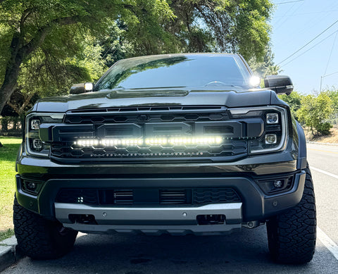 Front view of a black 2024 Ford Ranger Raptor showcasing hood mount LED lights on a sunny day.