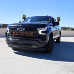 Black Chevrolet Silverado 1500 ditch lights PRO dual color LED upgrade on front bumper in sunny parking lot
