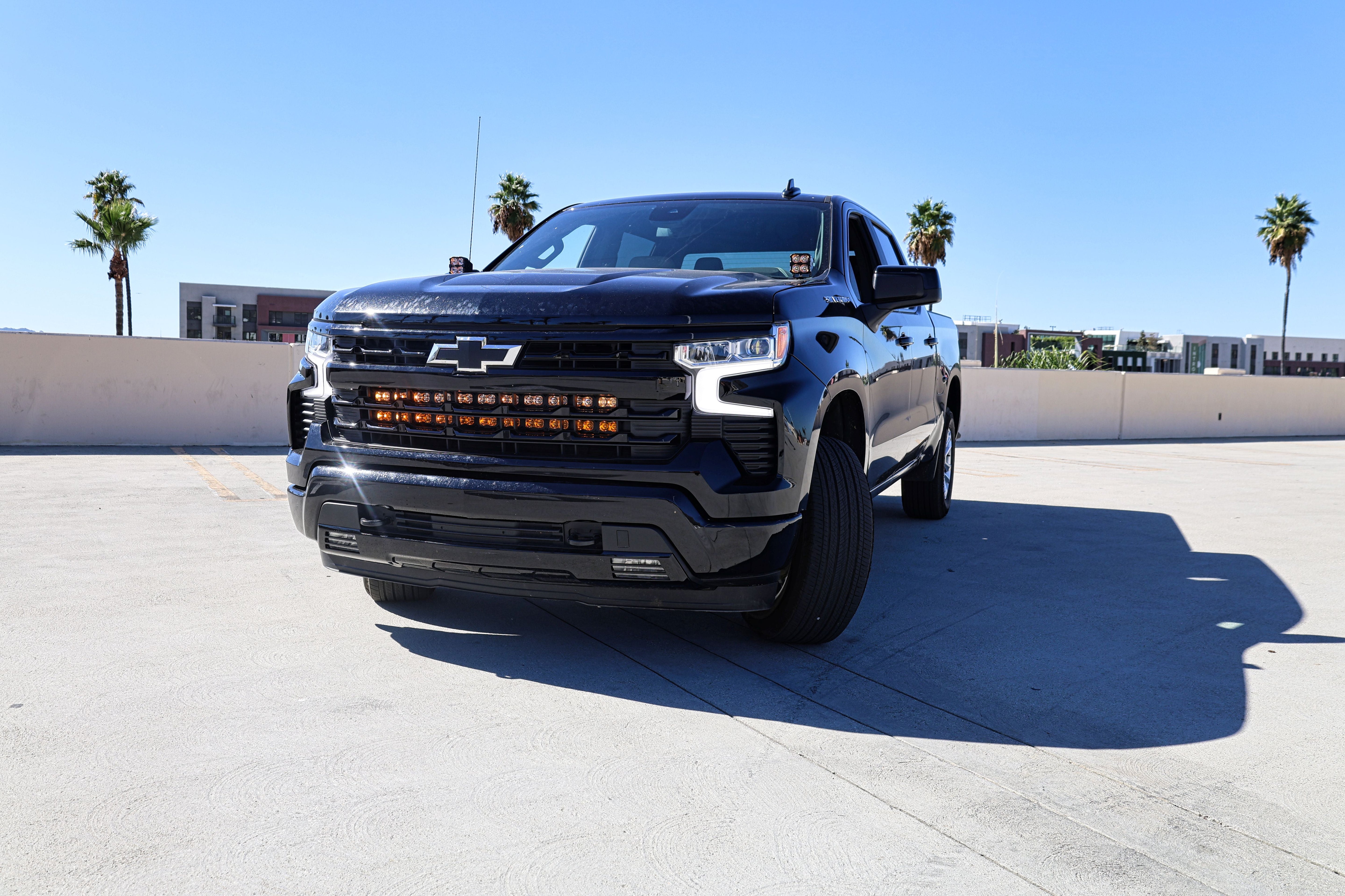 Black Chevrolet Silverado 1500 ditch lights PRO dual color LED upgrade on front bumper in sunny parking lot